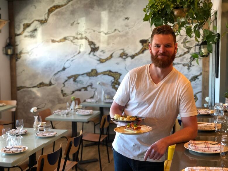 A man holding plates of food smiles as he lines against a bar in a restaurant.