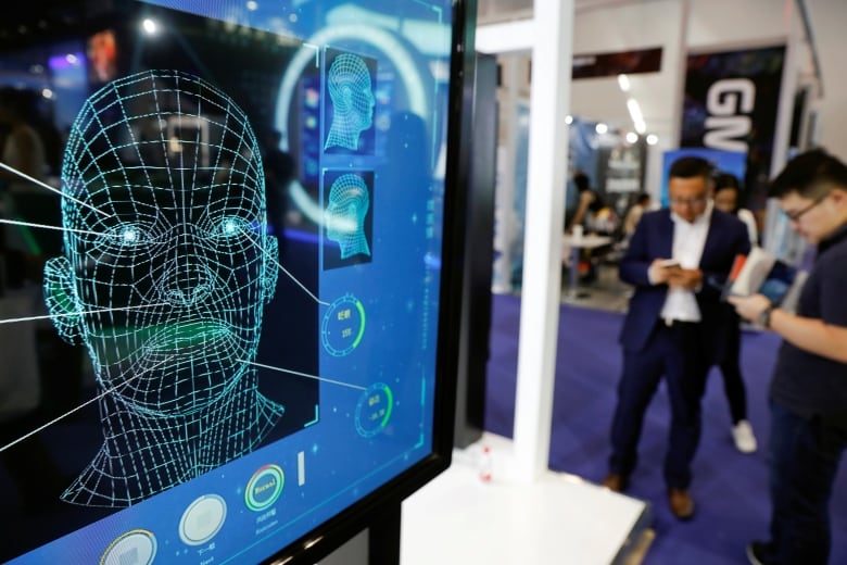 Visitors check their phones behind the screen advertising facial recognition software during Global Mobile Internet Conference (GMIC) at the National Convention in Beijing, China April 27, 2018.