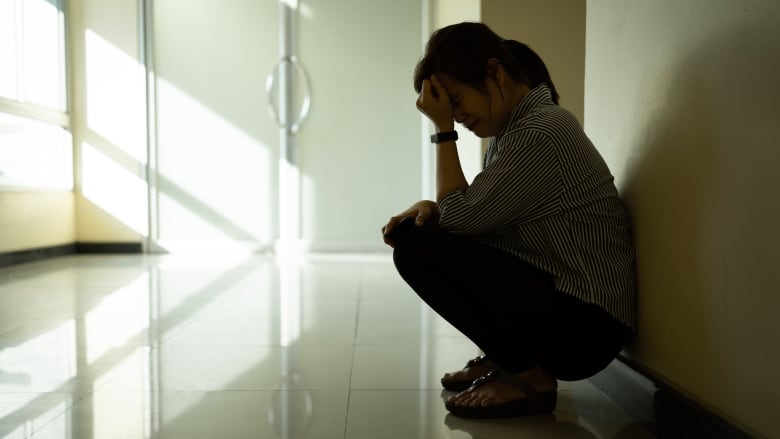 A woman in shadows holds her head in her hands.