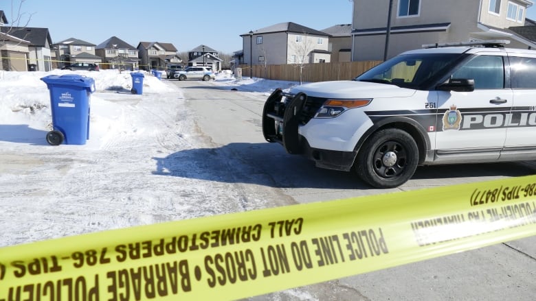 A police cruiser car and yellow police tape on a snowy residential street.