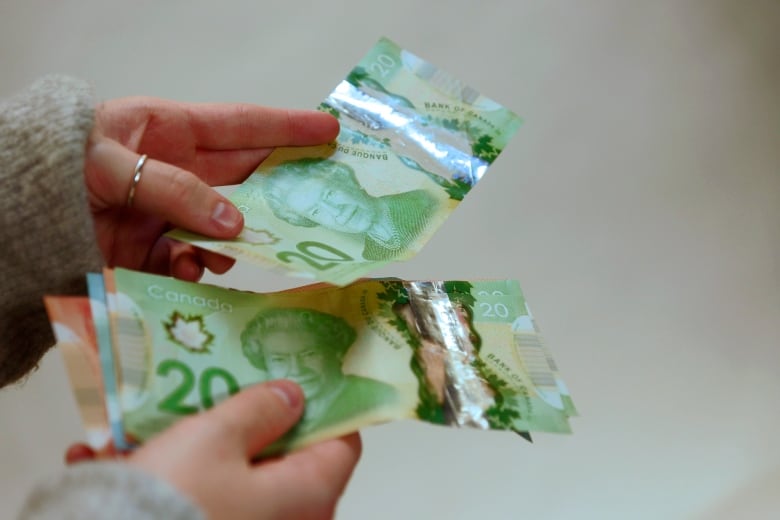 A closeup shows a person's hands holding cash, including two $20 bills.