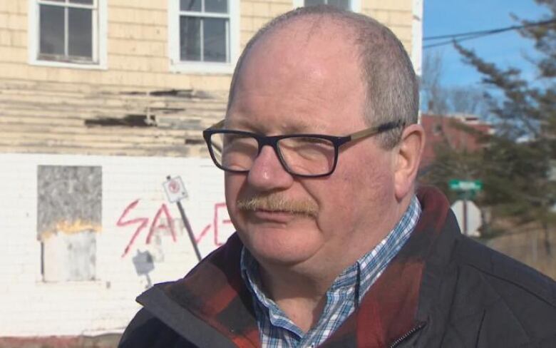 A white man with a mustache and black-rimmed glasses