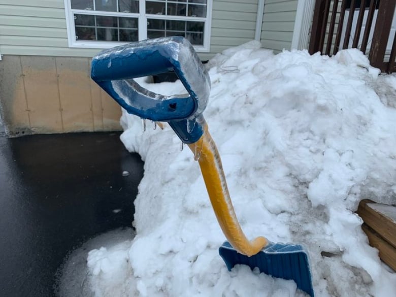 Ice covers the blue handle and yellow shaft of a shovel 