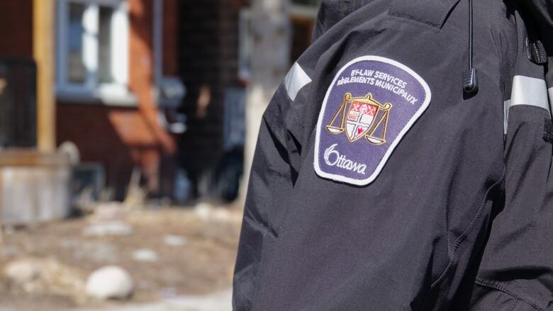 A close-up of a by-law services officer's shoulder, showing the City of Ottawa By-Law services crest. 