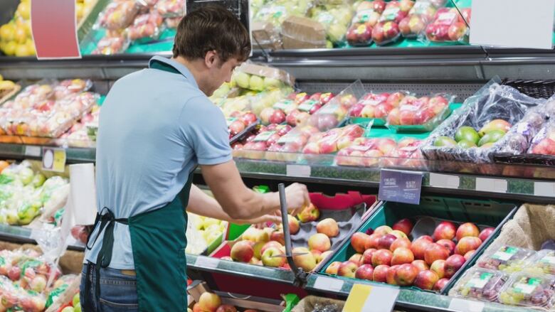 A man in an employee's apron sorts fruit in a grocery store aisle.