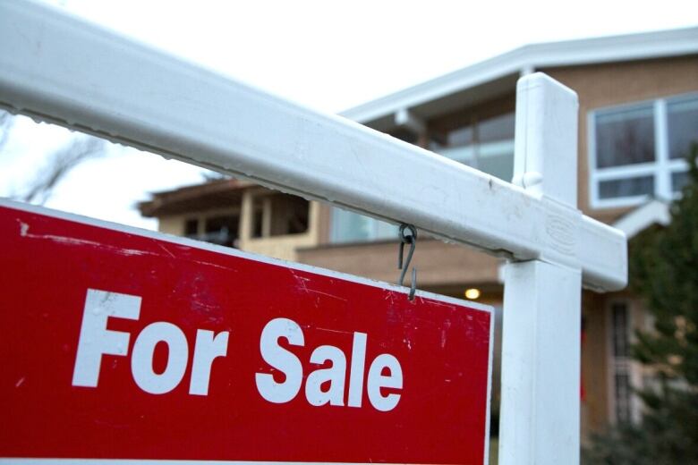 A red for sale sign is pictured in front of a property in the background. 