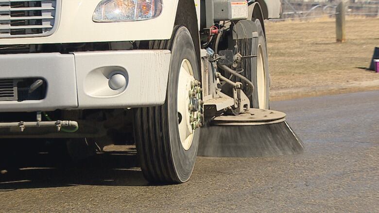 Close-up of front of street-sweeping truck, showing a brush in action with a damp road in the background.