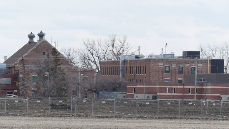 Exterior of a large, brown brick building surrounded by chain-link fencing