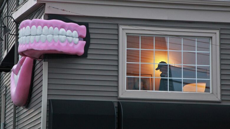 A grey building is shown with a large pair of teeth displayed on the corner advertising it as a denture clinic.