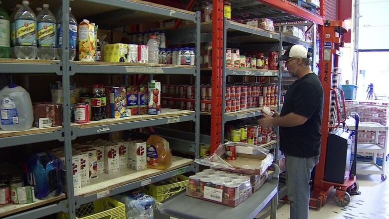 A man stands in front of a shelf of canned and packaged food. 