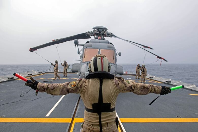 Ground crew store a military helicopter on the deck of a frigate.