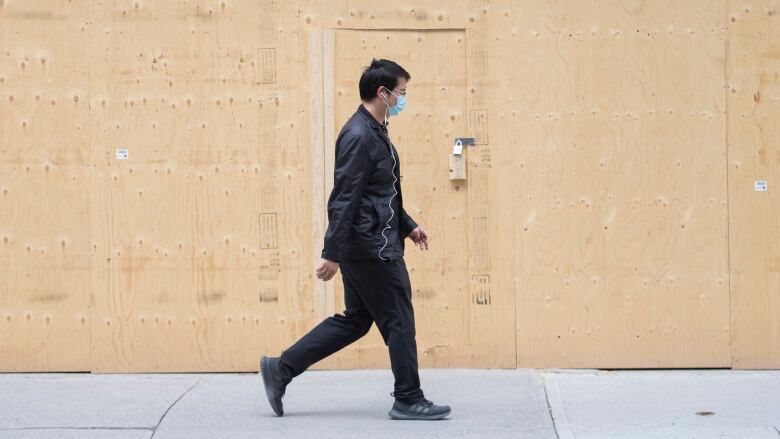 A man walks by a barricaded storefront. 