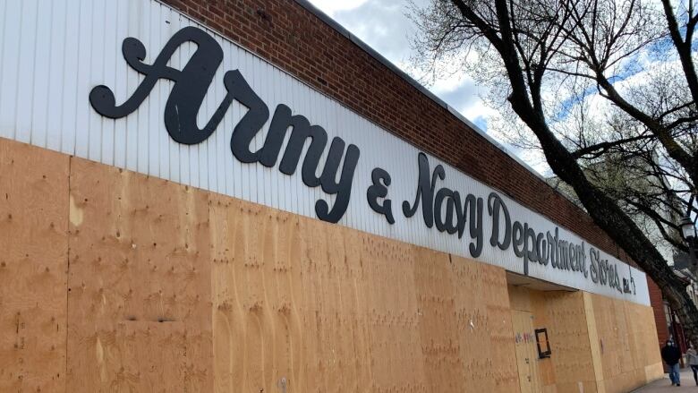 A view of a storefront from outside, on the sidewalk. The windows are boarded up with plywood.