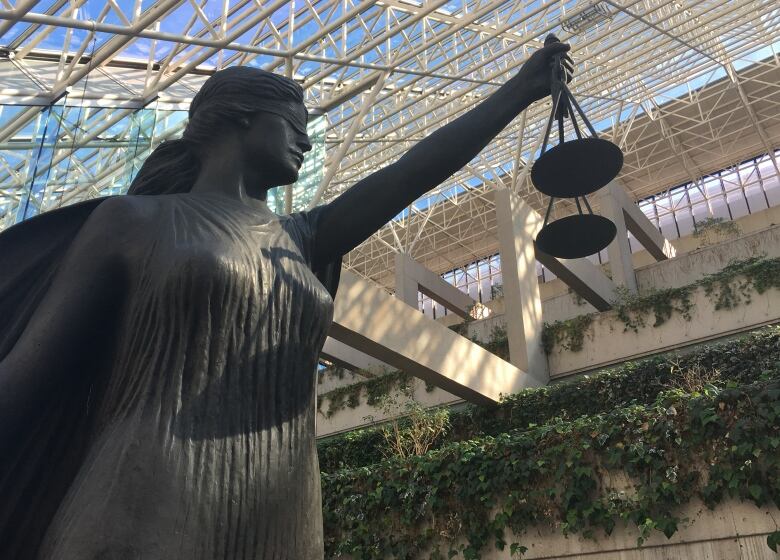 The scales of justice statue at B.C. Supreme Court with greenery and the buildings skylight roof in the background.