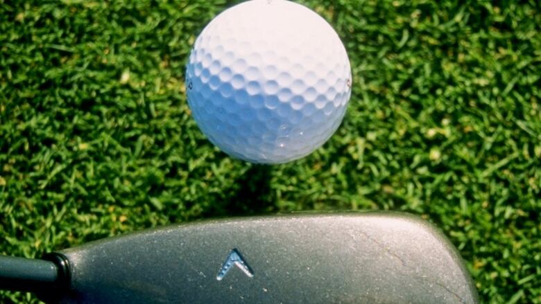 A close-up photo of golf ball about to be hit by a golf club.