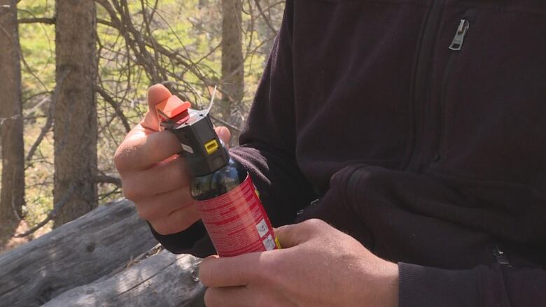 A close up of a person's hands, holding a red canister of bear spray.