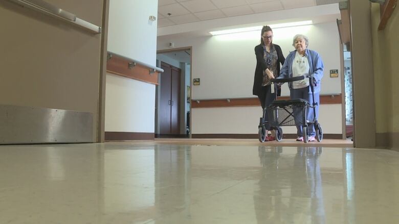 A personal support worker helps a senior walk down the hall.