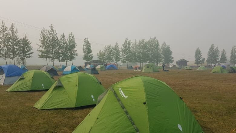 A number of tents pitched in a sports field with smoky skies overhead.