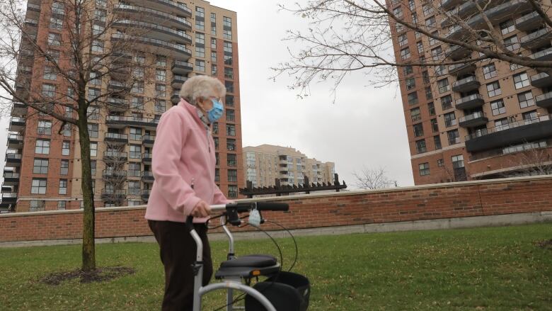 A woman with a walker is in a green space near tall buildings.