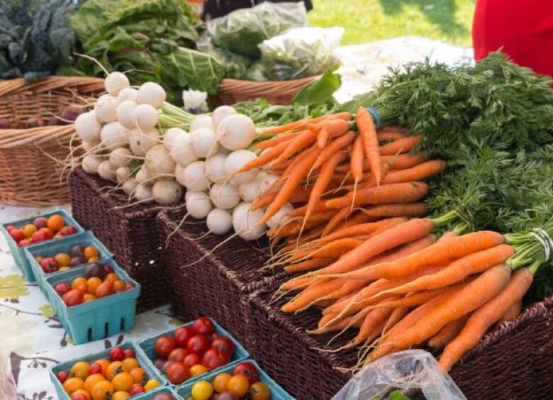 A table of produce at a farmers' market, featuring carrots, green onions and tomatoes.