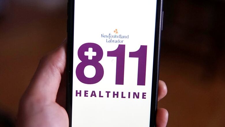 A hand holds an IPhone with the 811 Healthline logo on the screen.