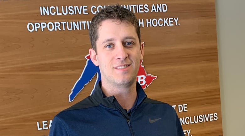 Man stands in front of Hockey New Brunswick sign.