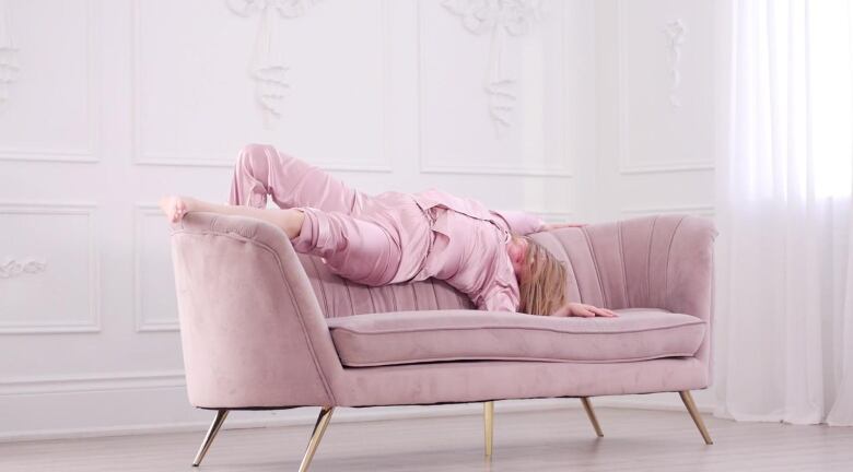 A woman wearing pink pajamas is splayed on a pink sofa.