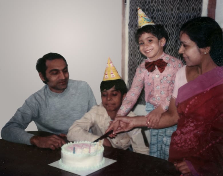 A family photo featuring four members celebrating a birthday party with a young kid slicing a cake. 