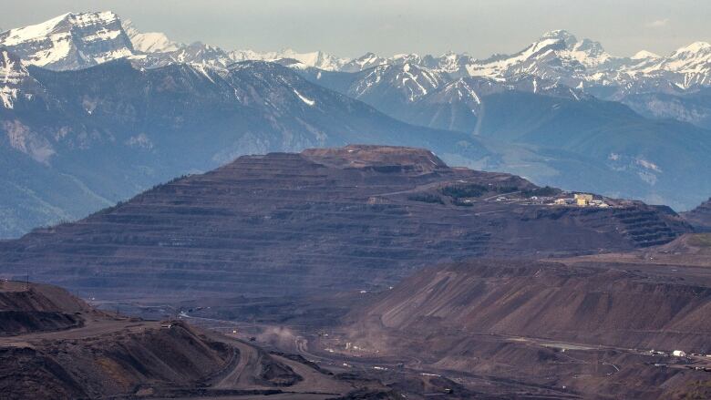 An open-pit mine is pictured with picturesque snowcapped mountains in the background.