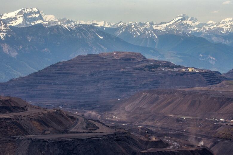 An open-pit mine is pictured with picturesque snowcapped mountains in the background.