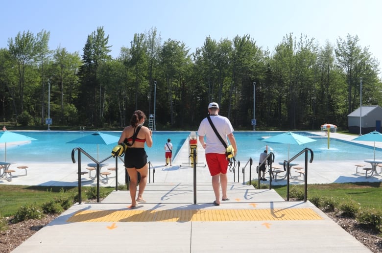 two people walk down a ramp toward a blue body of water 