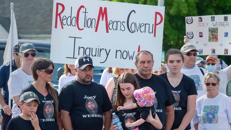 People in black T-shirts stand in front of picket signs at a protest.