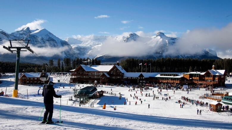 A person skis down a ski hill toward a building. 