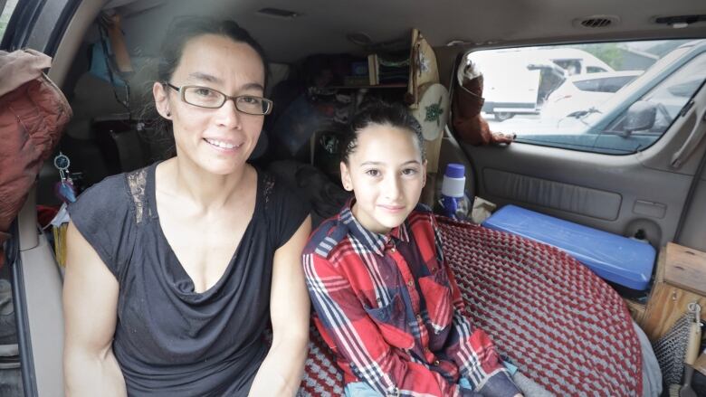 A woman and a young girl sit in the back of a minivan