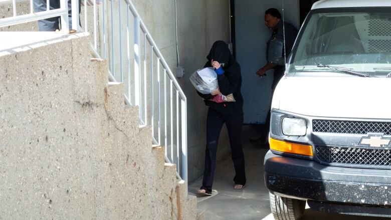 A woman wearing a black hoodie and black jeans tries to cover her face as she makes way toward stairs. 