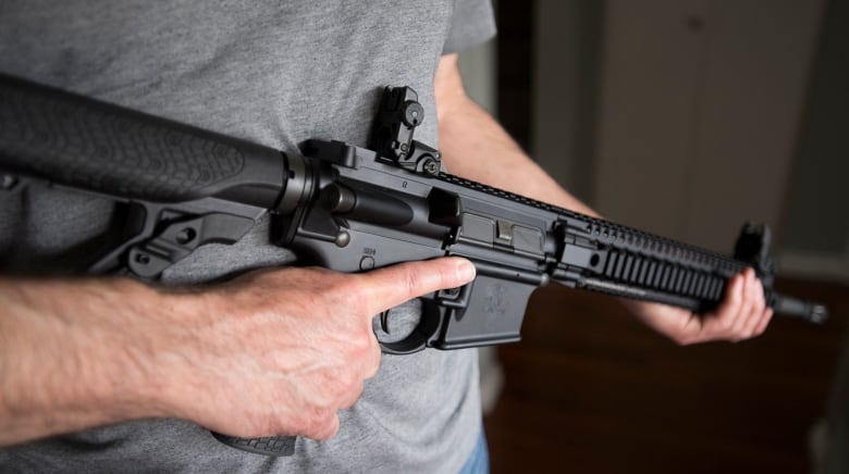 A man holds an AR-15 rifle.