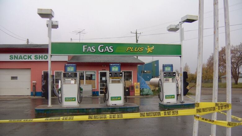 A Fas Gas Plus sign stands over a small salmon-coloured gas station with three gas pumps out front. Police is strung across the front of the parking lot.