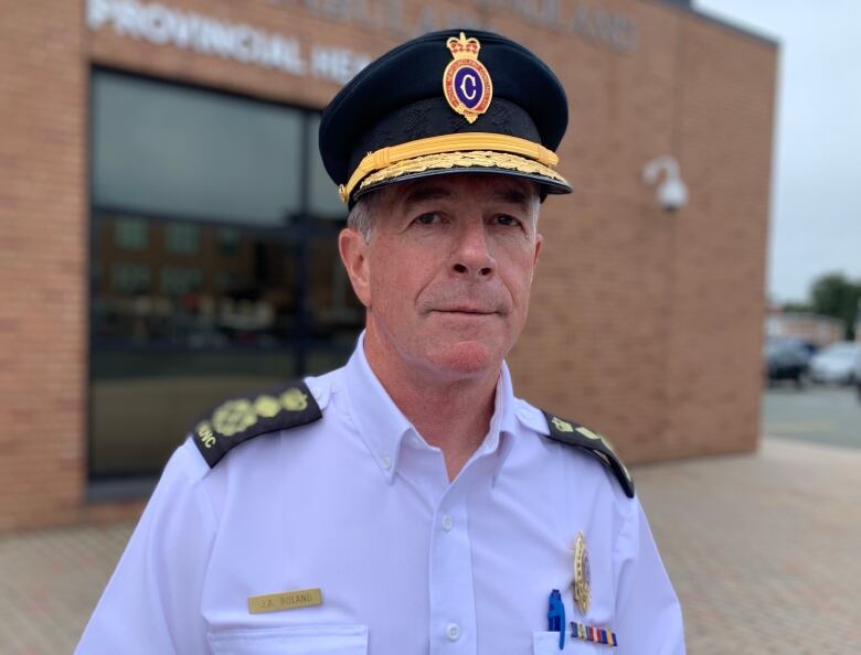 A man is wearing a white shirt and black hat bearing the Royal Newfoundland Constabulary's crest. 