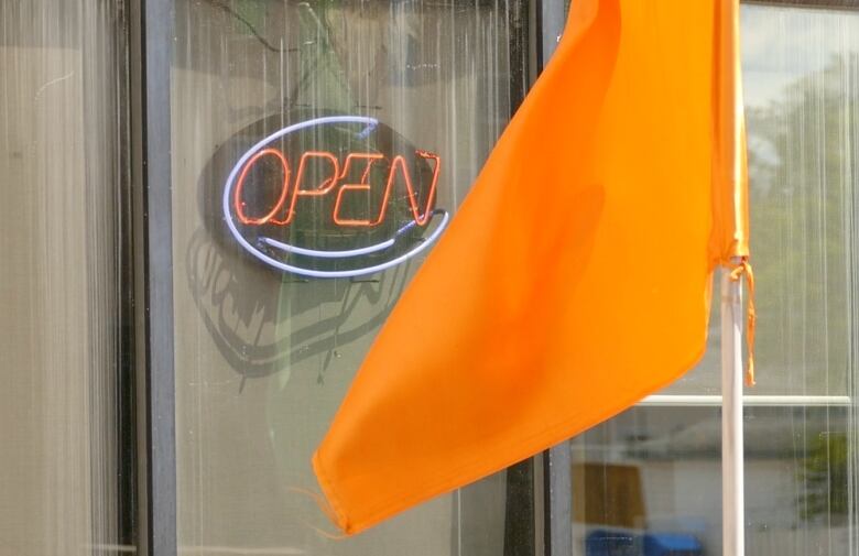 An orange flag hangs outside a business with a neon 