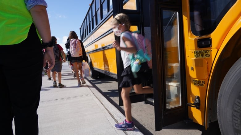 A student waring a respiratory mask leave a school bus at the start of a school year.