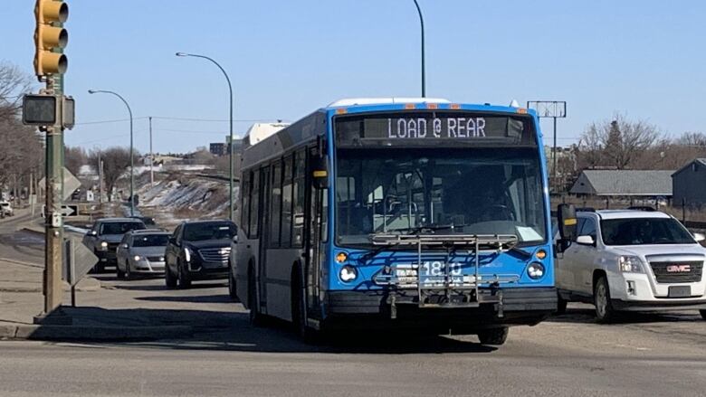 A blue bus heads up a road toward the camera.