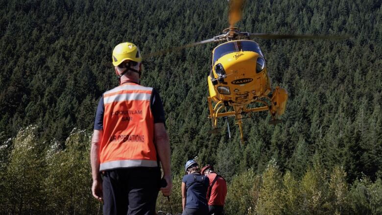 A man wearing a high-vis vest looks at a helicopter taking off.