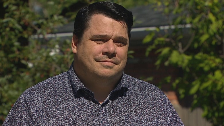 Craig Jenne is standing in front of trees and looking off camera