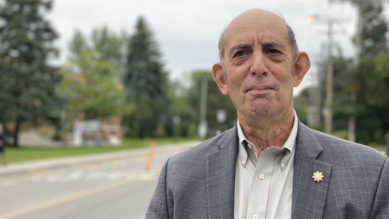 Marvin Rotrand stands on the street wearing a grey suit with a white shirt.