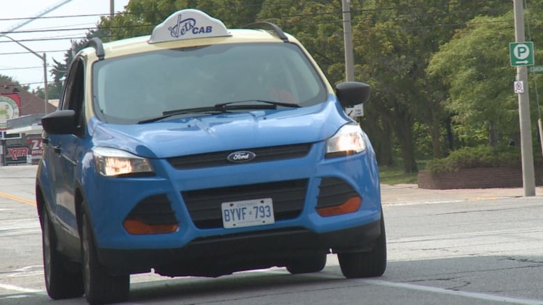 A blue and yellow cab drives down the street. 