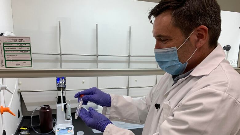 A scientist wearing a facemask handles test tubes. 