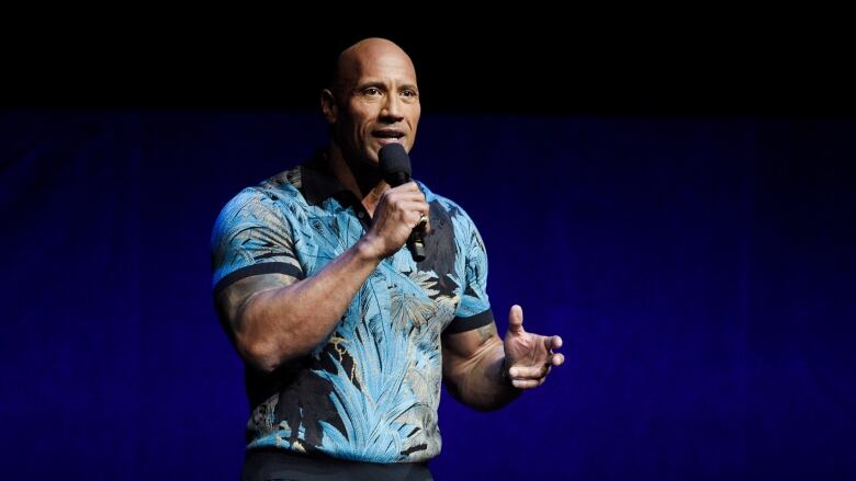 Dwayne Johnson holds a microphone.