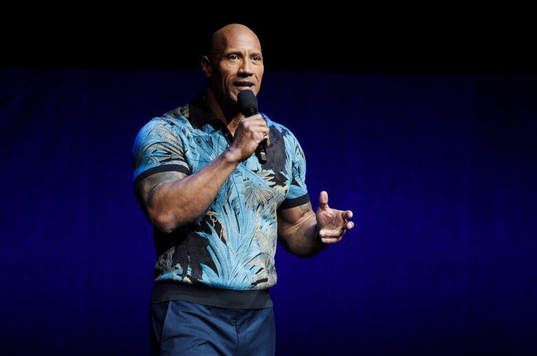 Dwayne Johnson holds a microphone.