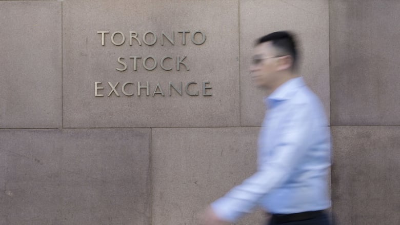 A man walks past a sign for the Toronto Stock Exchange. 