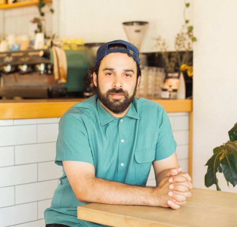 A bearded man wearing a teal shirt and backwards cap.